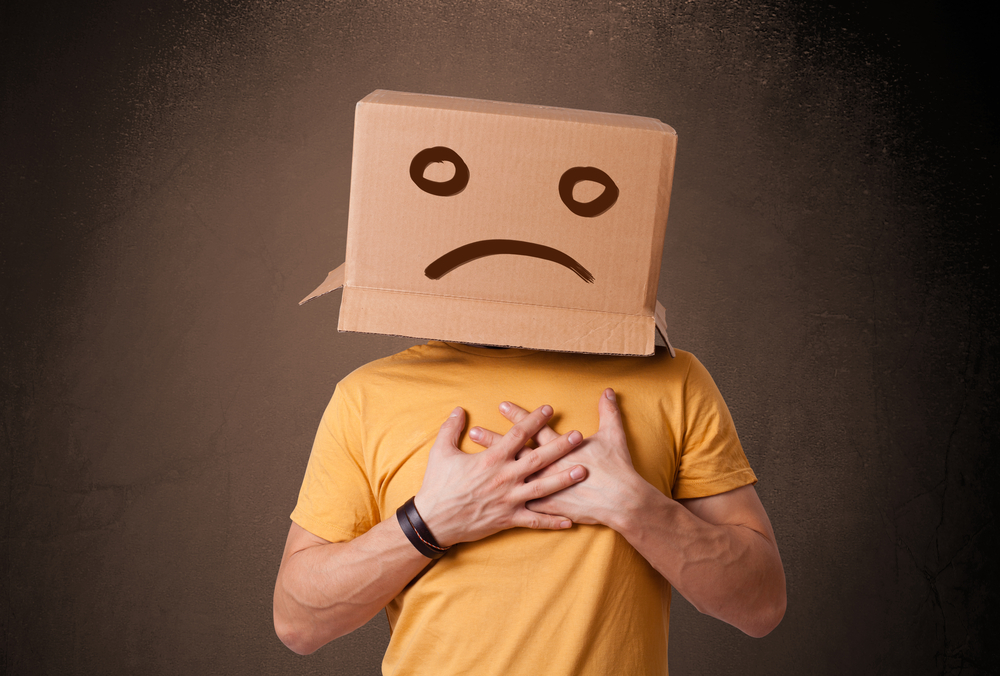 Young man standing with a brown cardboard box on his head with sad face